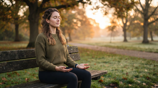 A woman sitting calmly on a park bench at sunrise, taking a slow breath