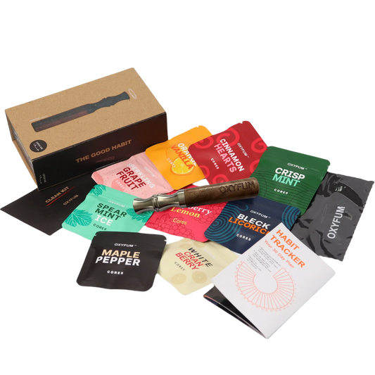 OXYFUM "The Good Habit" kit laid out: a wooden inhaler with kraft box, a clean kit cloth, a habit tracker booklet, and essential-oil flavor core packets including Grape Fruit, Orange Vanilla, Cinnamon Hearts, Crisp Mint, Spearmint Ice, Cherry, Lemon, Black Licorice, Maple Pepper and White Berry.